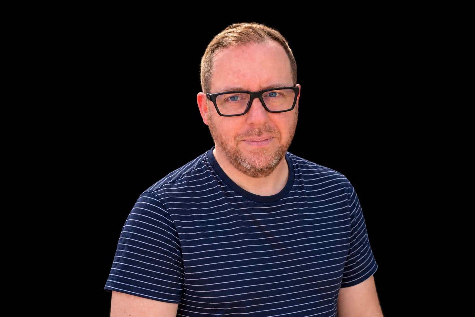 Darren Wells, smiling, wearing glasses and a navy striped T-shirt.